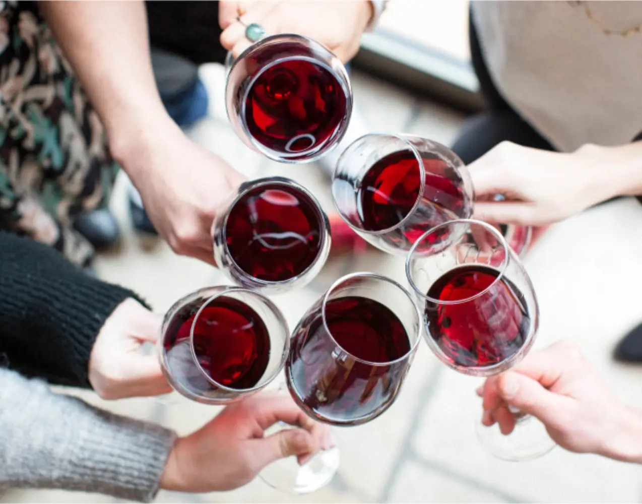 Overhead view of six hands raising glasses of red wine together over a table