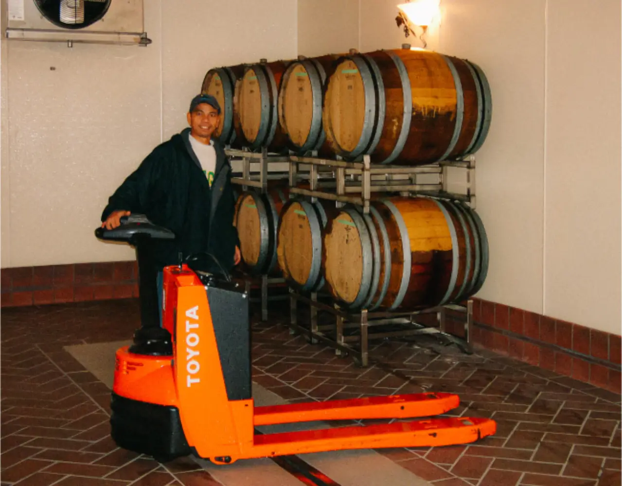 A Sweet Cheeks cellar hand beside stacked oak wine barrels in the winery barrel room